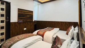 A hotel room with a modern design, featuring a wooden headboard, a bed with multiple pillows, and a ceiling with recessed lighting and a fan. - S R HOTEL (Varanasi)