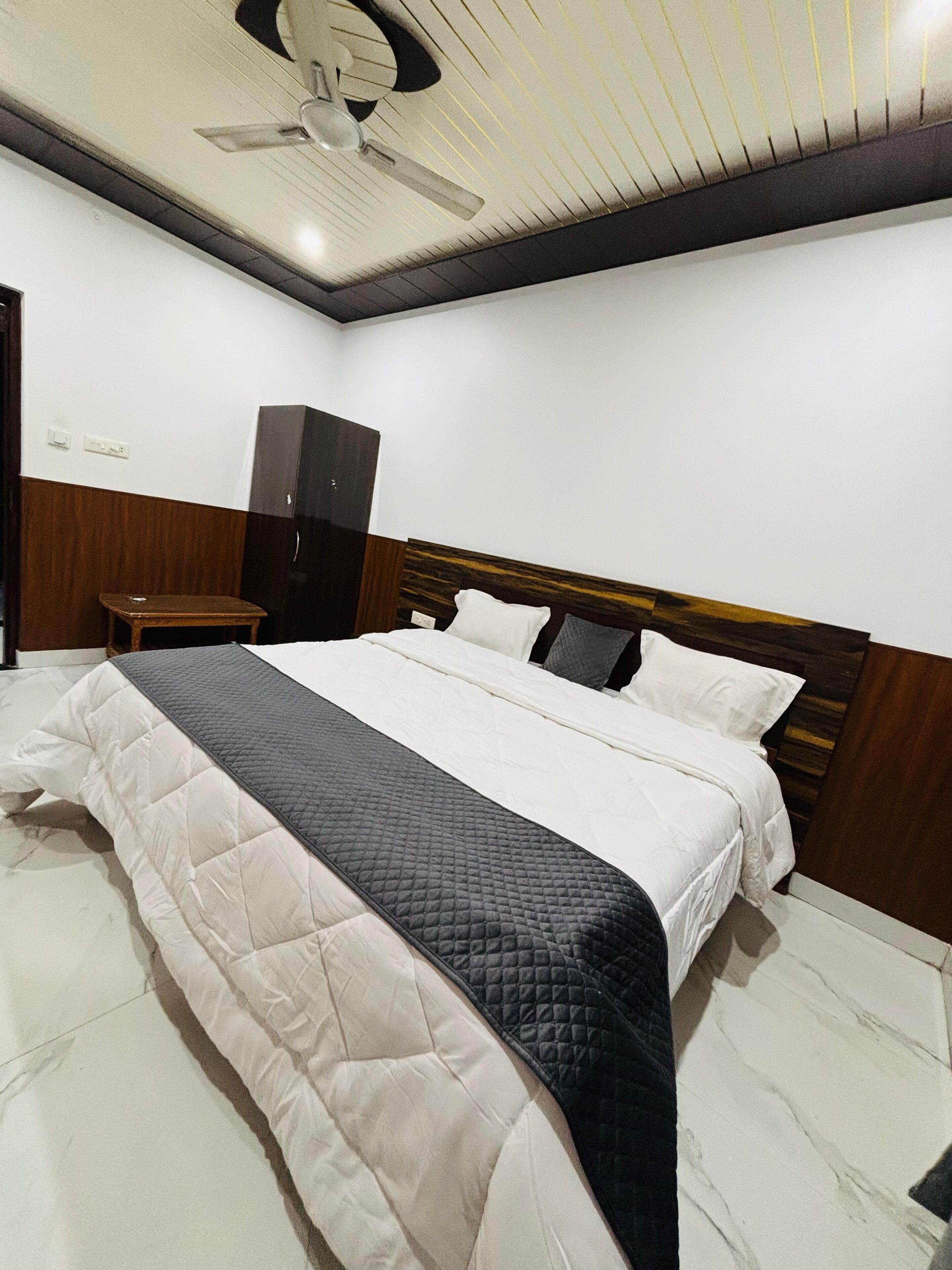 A neatly made bed with a quilted bedspread, a wooden headboard, and a ceiling fan.