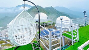 A hanging chair, a greenhouse, and a white fence in a garden with a mountainous backdrop. - HR 26 Hotels & Resorts (Rishikesh)