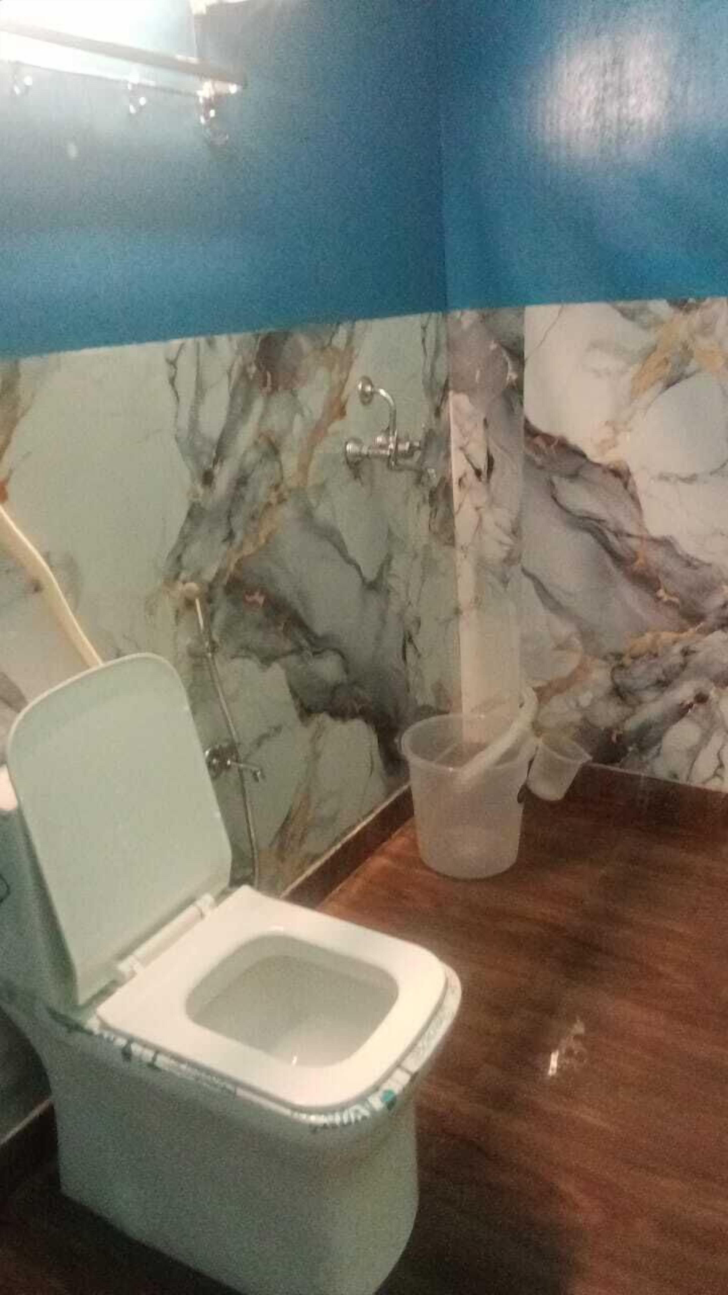 A bathroom with a marble wall, a toilet, and a shower area.