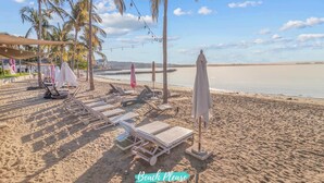 Una playa con sillones de playa, sombrillas y palmeras.