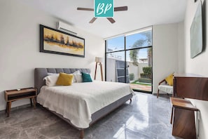 Une chambre à coucher moderne avec un grand lit, un ventilateur de plafond, un tableau et une vue sur l’extérieur.