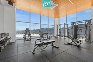 A gym with various exercise equipment, large windows, and a view of a mountainous landscape.