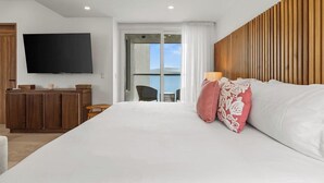 A hotel room with a large bed, a flat-screen TV mounted on the wall, a wooden headboard, and a balcony with a view.