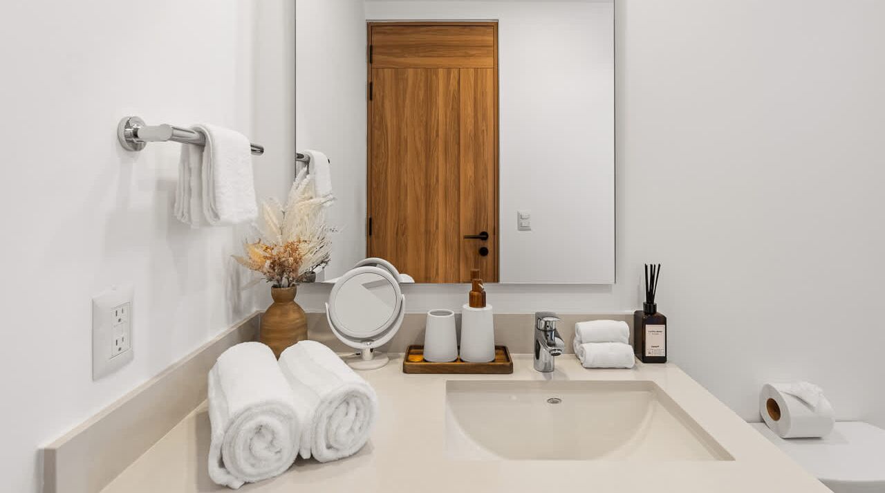 Un baño con puerta de madera, un lavabo blanco, un espejo y toallas.