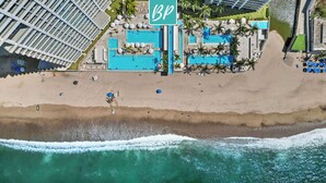 An aerial view of a beach resort with multiple swimming pools, a large 'BP' sign, and a sandy beach.