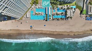 An aerial view of a beach resort with multiple swimming pools, a large 'BP' sign, and a sandy beach. - Beachfront Studio • Rooftop Pool • Ocean Views (Puerto Vallarta)