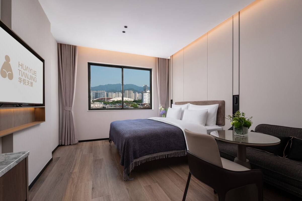 Una habitación de hotel moderna con una cama grande, un escritorio, un sofá y vistas a la ciudad.