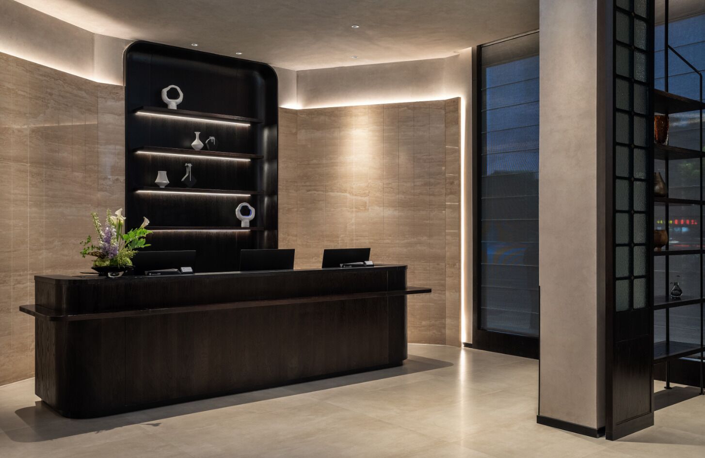 A reception desk with a dark wood finish, a vase with flowers, and a modern shelving unit with decorative items.