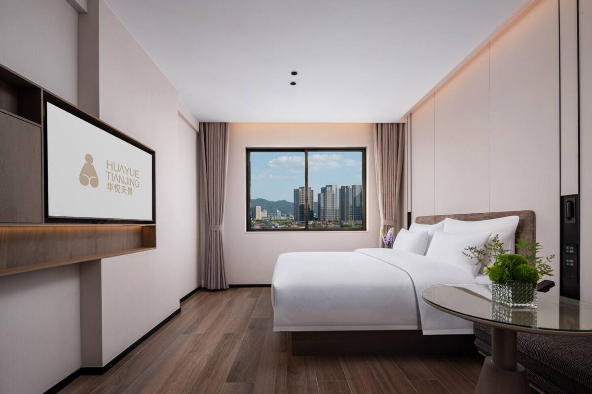 Habitación de hotel con cama, mesa de vidrio, televisor en la pared y vista a la ciudad.