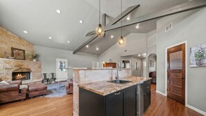 A spacious living area with a fireplace, leather sofa, and a kitchen island with a sink. - 2 Home Getaway-Pool-Hot Tub-Pickleball Court (Fredericksburg)