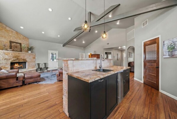 A spacious living area with a fireplace, leather sofa, and a kitchen island with a sink.