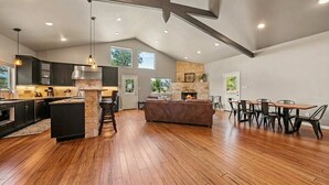 A spacious kitchen with a stone fireplace, wooden flooring, and a dining area with chairs and a table. - 2 Home Getaway-Pool-Hot Tub-Pickleball Court (Fredericksburg)