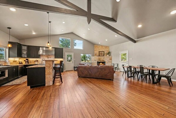 A spacious kitchen with a stone fireplace, wooden flooring, and a dining area with chairs and a table.