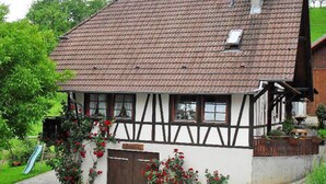 Une maison traditionnelle à colombages, dotée d’un toit en pente, d’une porte d’entrée et d’un petit jardin agrémenté d’un sentier.