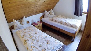 Une chambre avec deux lits simples, une tête de lit en bois et une petite table de chevet sur laquelle se trouve un livre.
