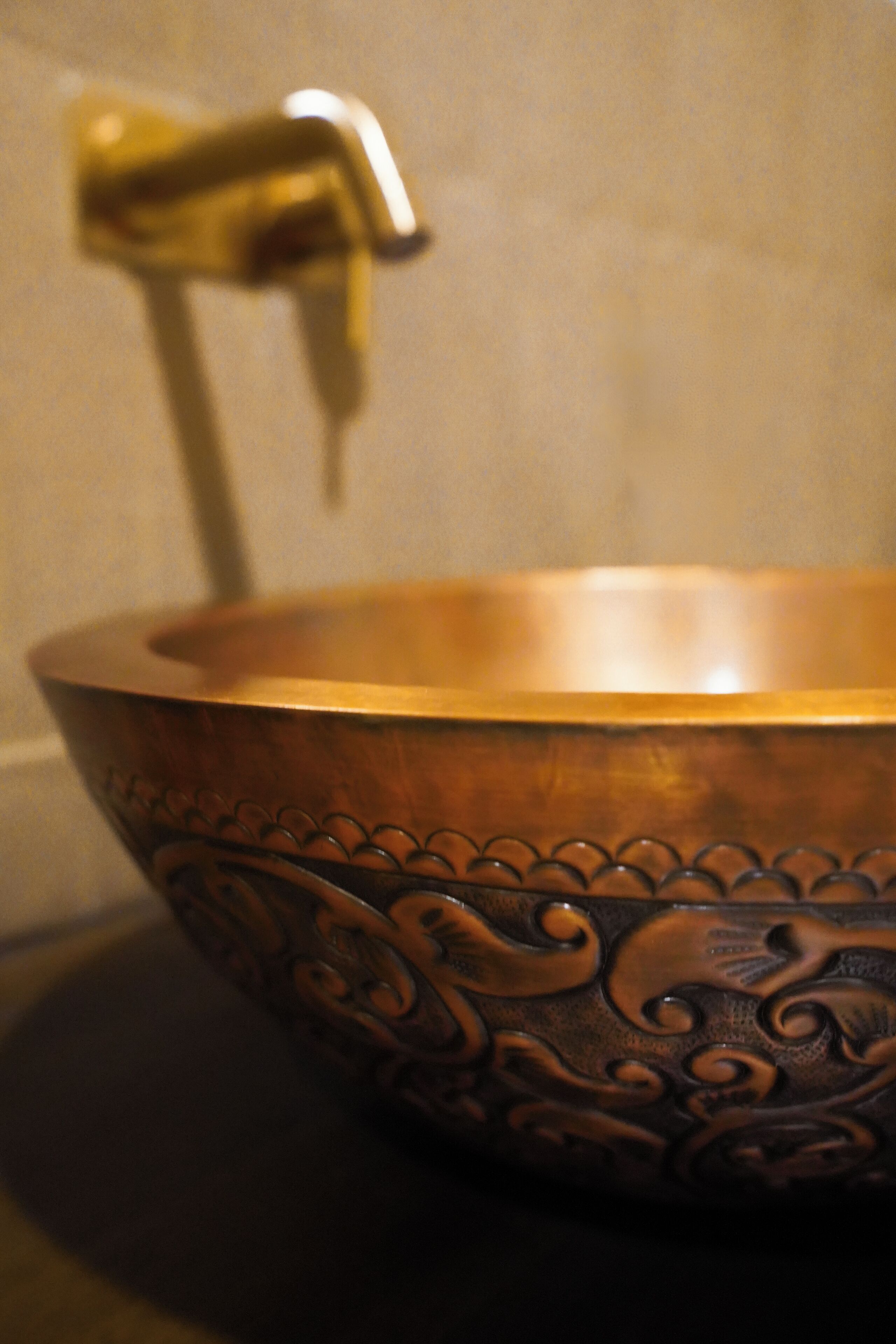 A copper basin with intricate designs, placed on a tiled surface.