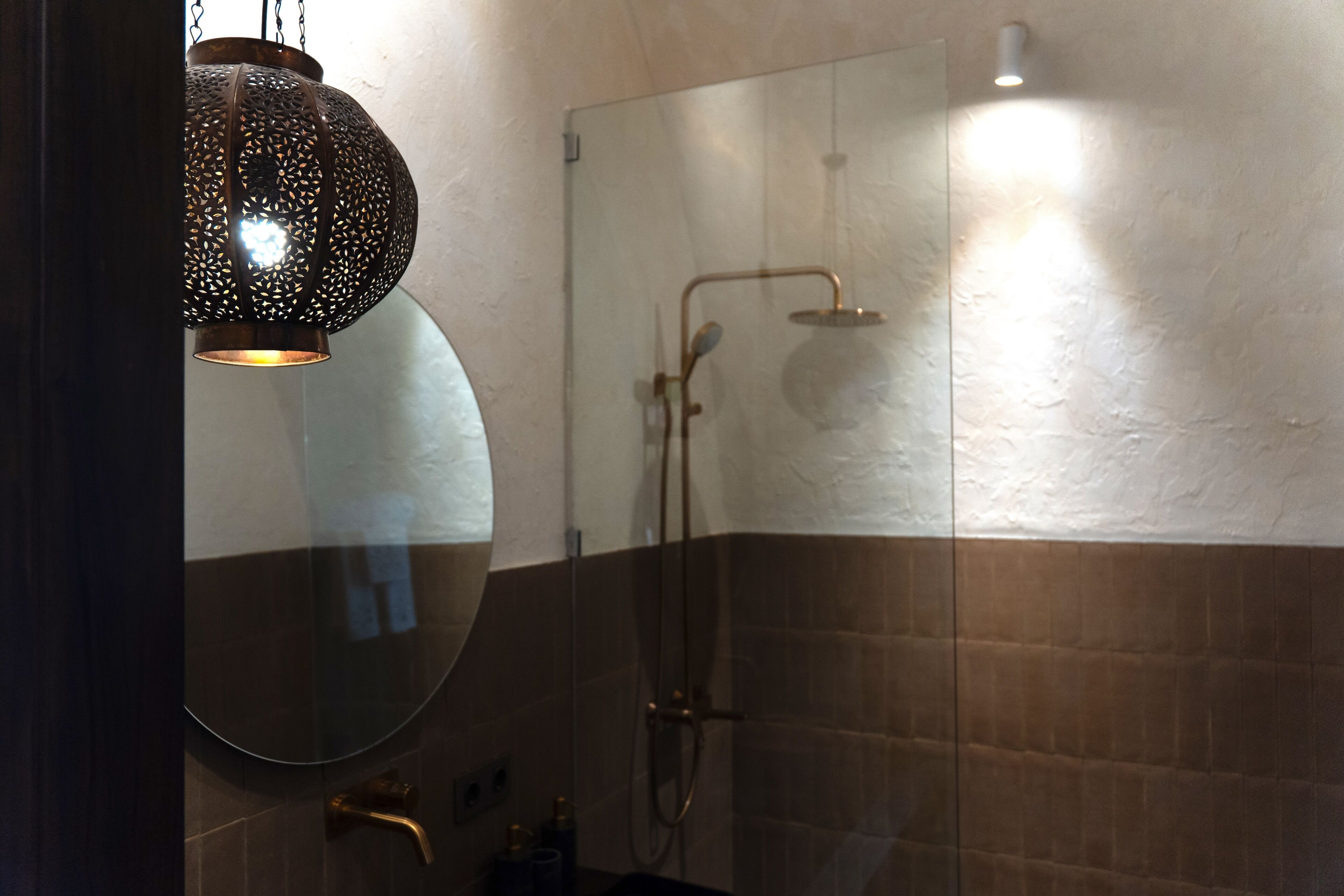 A modern bathroom with a glass shower enclosure, a round mirror, and a hanging light fixture.