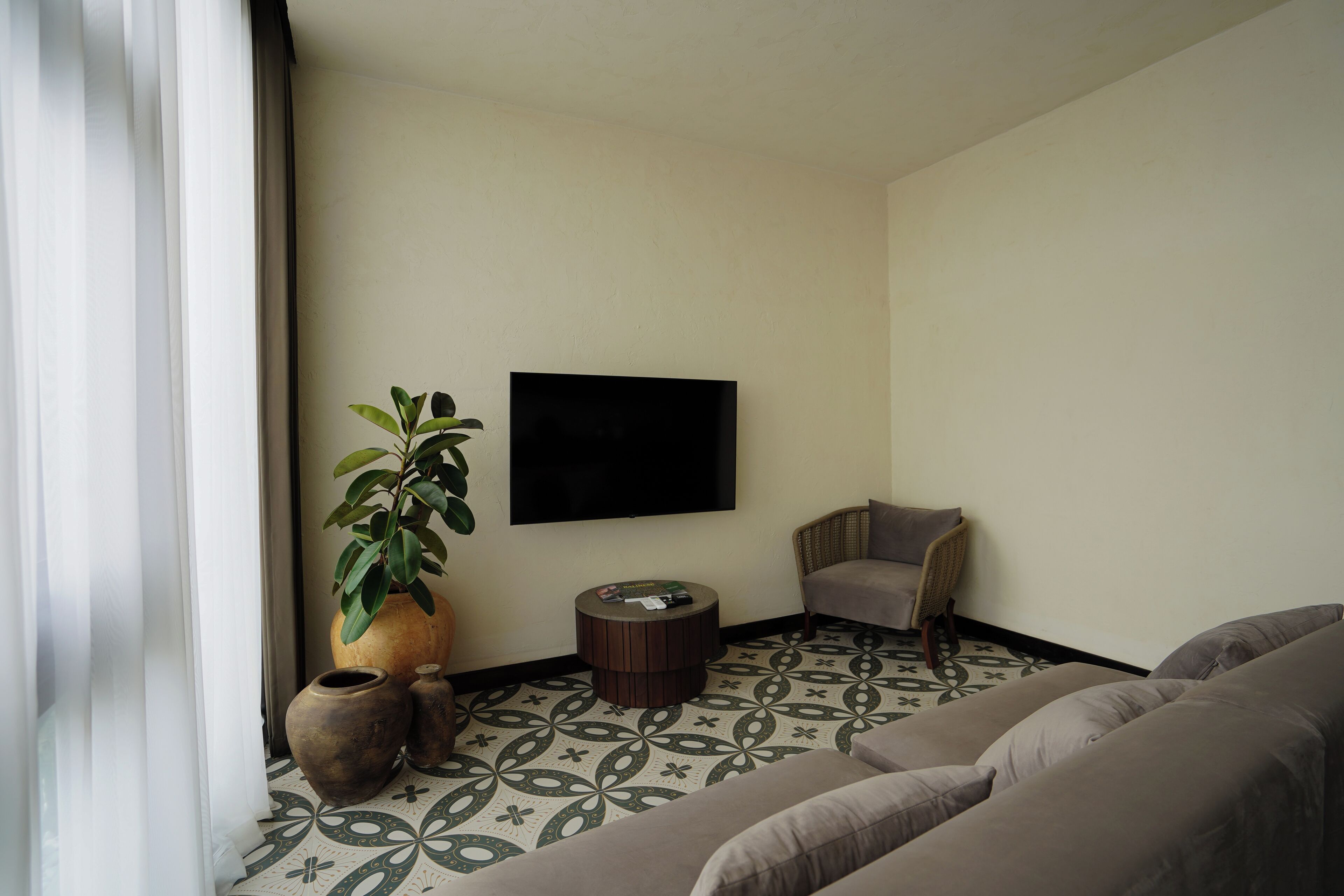 A living room with a sofa, a chair, a TV mounted on the wall, and a patterned floor.