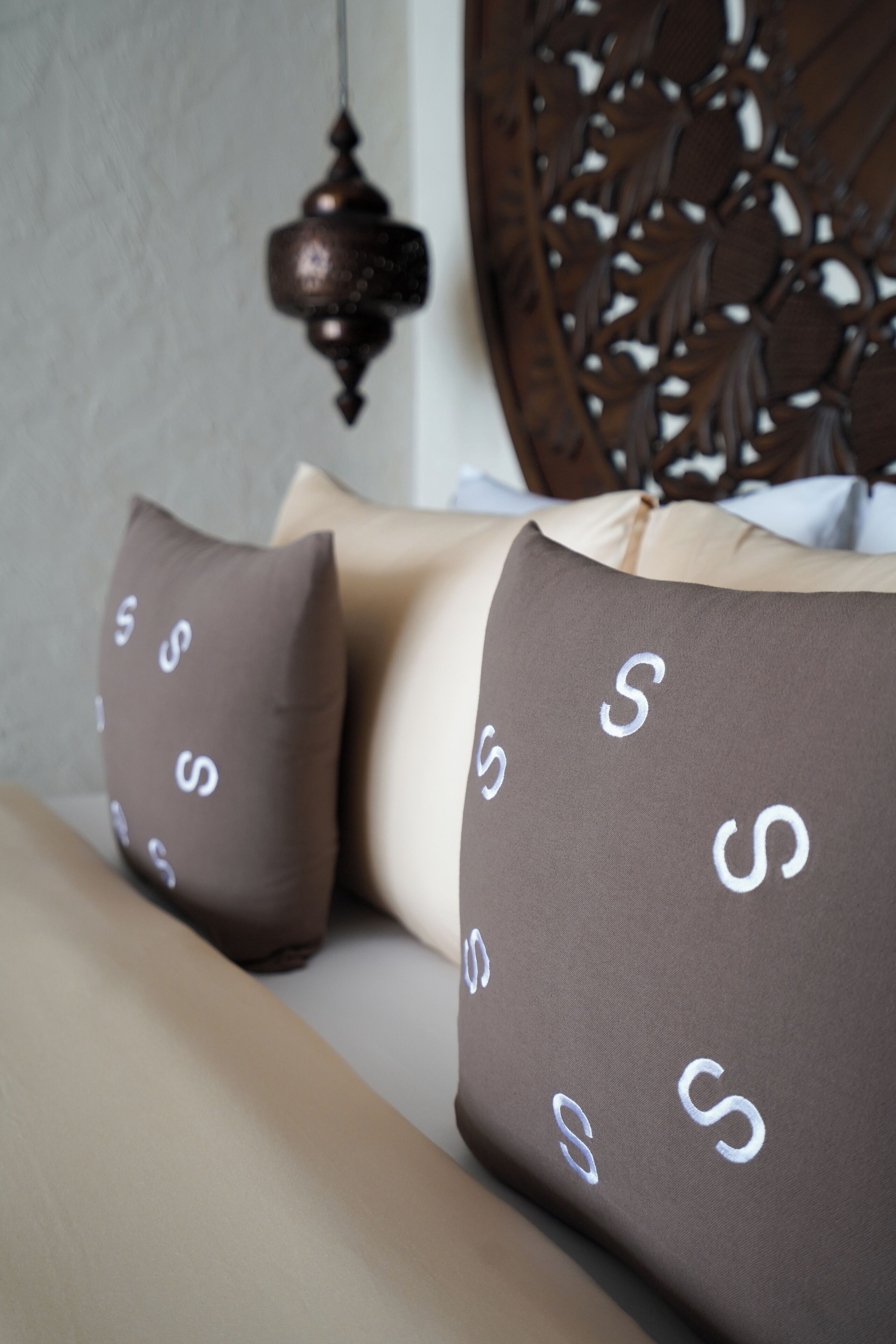 Una cama con cabecera, dos almohadas estampadas y una lámpara colgante.