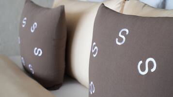 Una cama con cabecera, dos almohadas estampadas y una lámpara colgante.