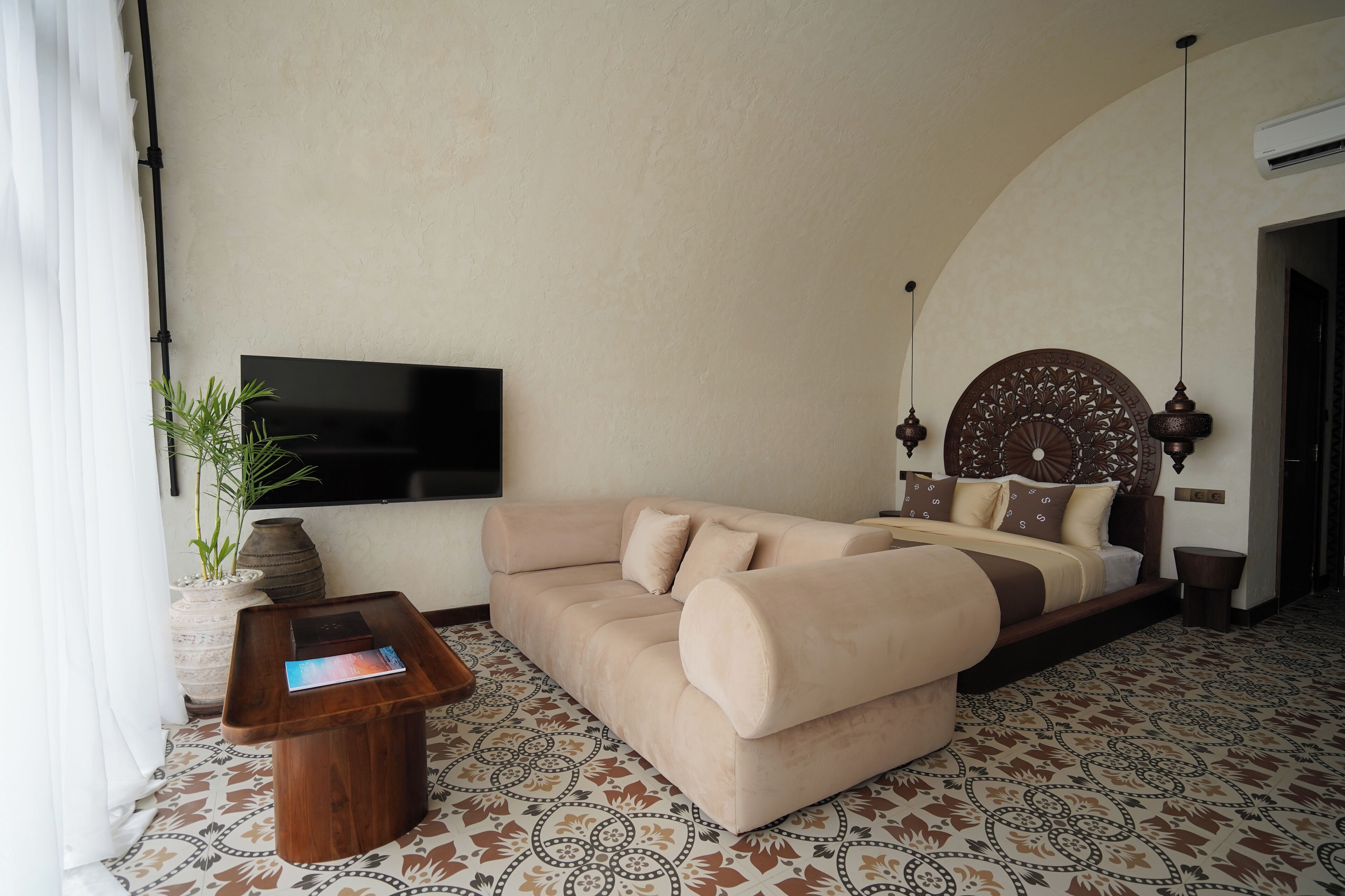 A modern bedroom with a sofa bed, a flat-screen TV, a decorative headboard, and a patterned floor.
