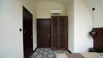 A narrow hallway with a patterned floor, a wooden door, a wardrobe, and an air conditioning unit mounted on the wall.