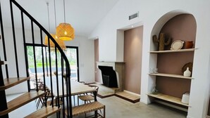 Un intérieur moderne avec un escalier en bois, un coin repas, une cheminée et une bibliothèque.