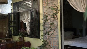 Une pièce avec un lit, une fenêtre avec des rideaux, une plante en pot et un mur en briques.