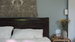 Une chambre à coucher avec un grand lit, une tête de lit, une table de chevet ornée d’un vase de fleurs et une décoration murale.