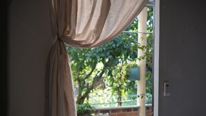 Une vue à travers une fenêtre avec des rideaux, un mur de briques et de la verdure à l’extérieur.