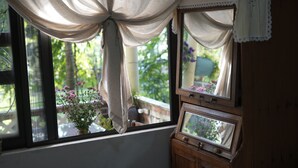 Une fenêtre avec un rideau, un meuble en bois et une plante en pot avec des fleurs.