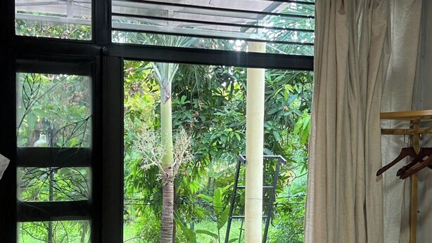 Une pièce dotée d’une grande fenêtre donnant sur un jardin luxuriant, un mur en briques et une étagère en bois.