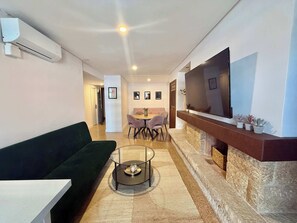A modern living room with a sofa, a coffee table, a fireplace, a TV, and a dining area with chairs and a table.