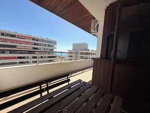 A balcony with wooden benches, a view of a modern building, and a clear sky.