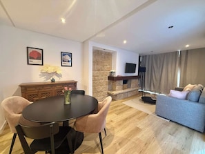 A modern living room with a fireplace, a sofa, a TV mounted on the wall, and a dining area with a table and chairs.
