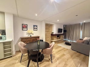 A modern living room with a dining area, stone fireplace, flat-screen TV, and a sofa.