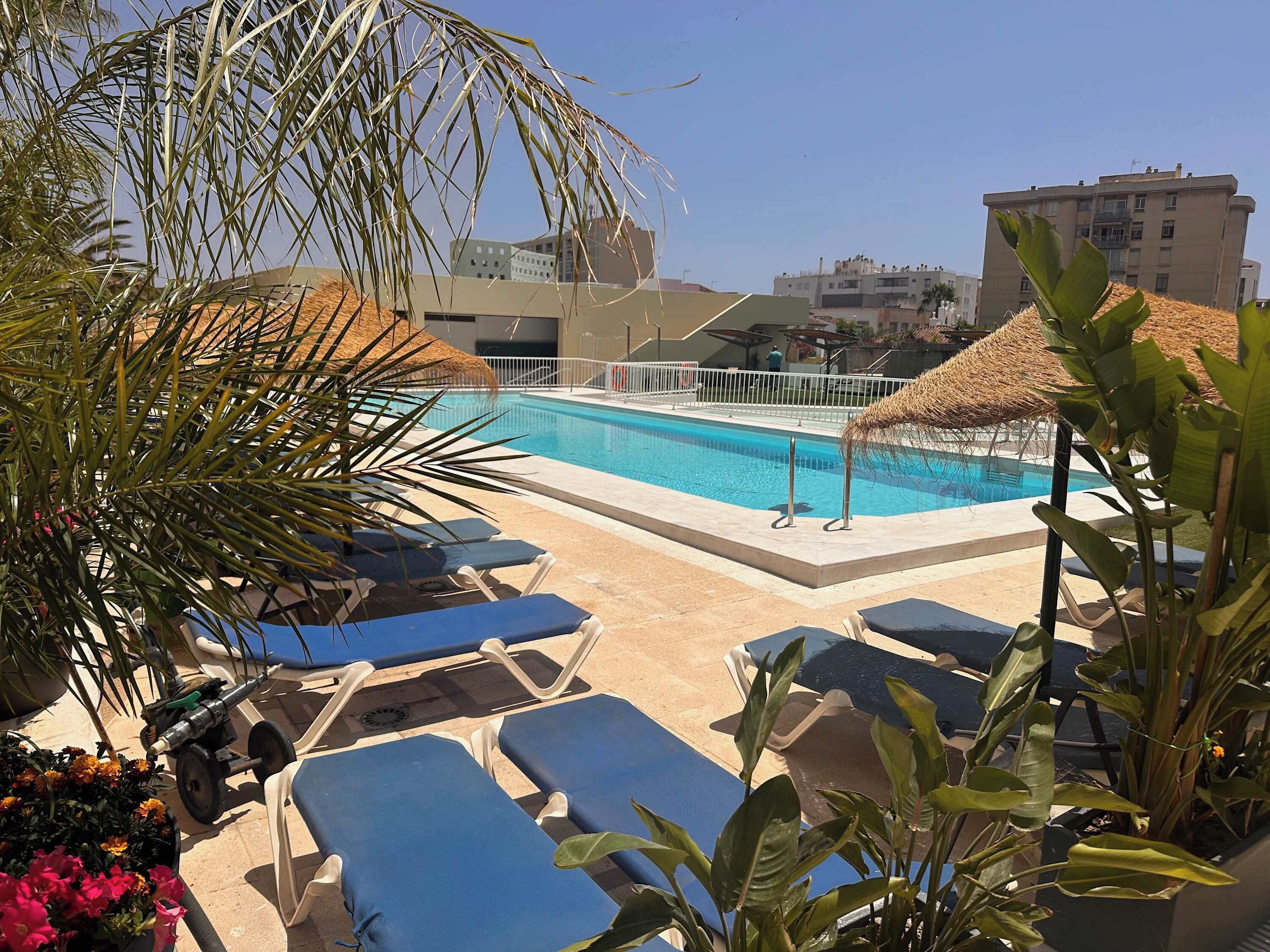 A pool area with lounge chairs and a thatched umbrella.