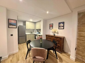 A compact kitchen with modern appliances, a dining area with a round table and chairs, and a small cabinet with decorative items. - Nogalera- Apartamento reformado (Torremolinos)