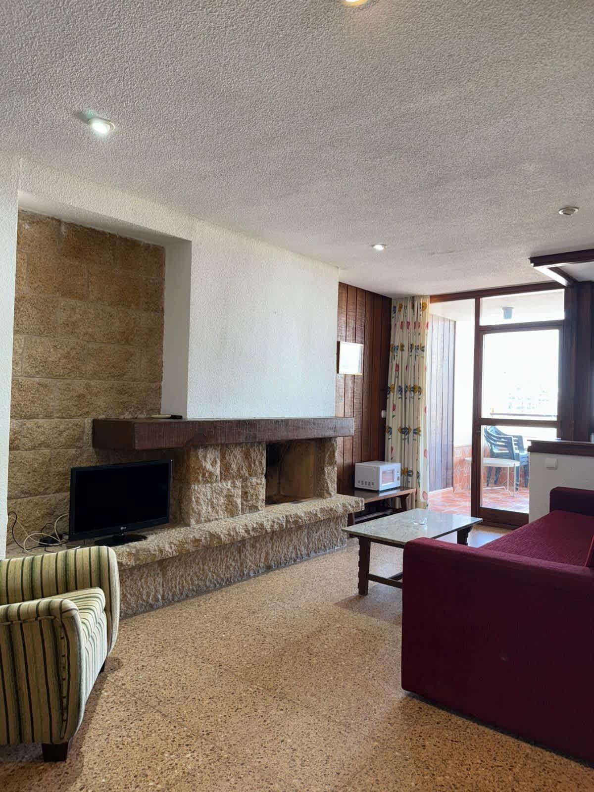 A living room with a stone fireplace, a flat-screen TV, a sofa, and a table.