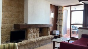 A living room with a stone fireplace, a flat-screen TV, a sofa, and a table. - Cozy apartment with terrace and views (Torremolinos)