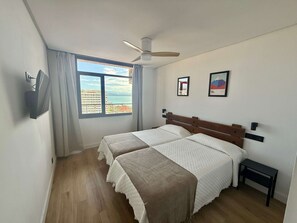 A bedroom with a bed, a ceiling fan, a window with curtains, and two framed pictures on the wall.