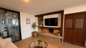Ein Wohnzimmer mit einer Couch, einem Couchtisch, einem Kamin, einem Fernseher und einer Schiebetür zu einem Schlafzimmer.