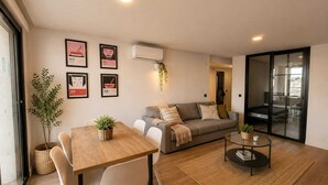 Ein modernes Wohnzimmer mit einer Couch, einem Esstisch mit Stühlen, einem Couchtisch und einer Glasschiebetür, die auf einen Balkon führt.