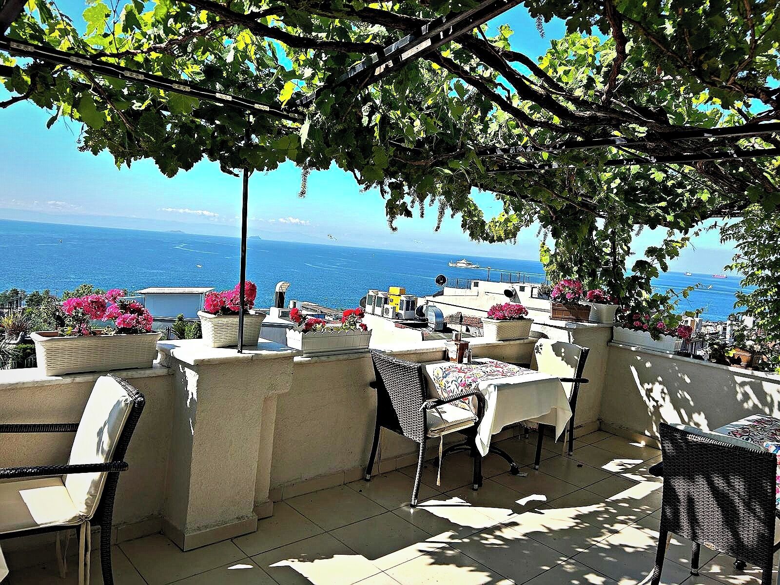 An outdoor terrace with tables and chairs, overlooking the sea.