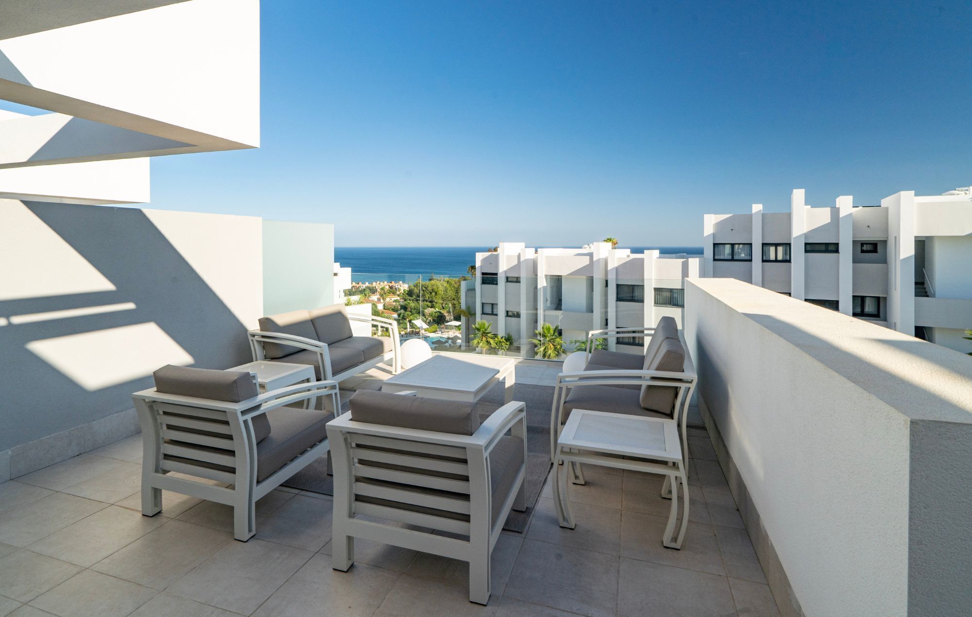 Eine Dachterrasse mit weißer Möbel, freier Meerblick und moderne Gebäude im Hintergrund.