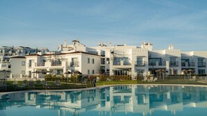 A modern hotel with a swimming pool, multiple balconies, and a clear sky.