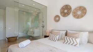 A modern bedroom with a large bed, a bedside table with a lamp, and a glass-enclosed shower area.
