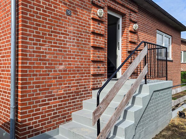 A red brick building with a number 10 sign, a door, and a staircase with a metal railing.