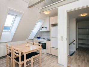 A compact kitchen with a dining table, chairs, a stove, and a refrigerator.